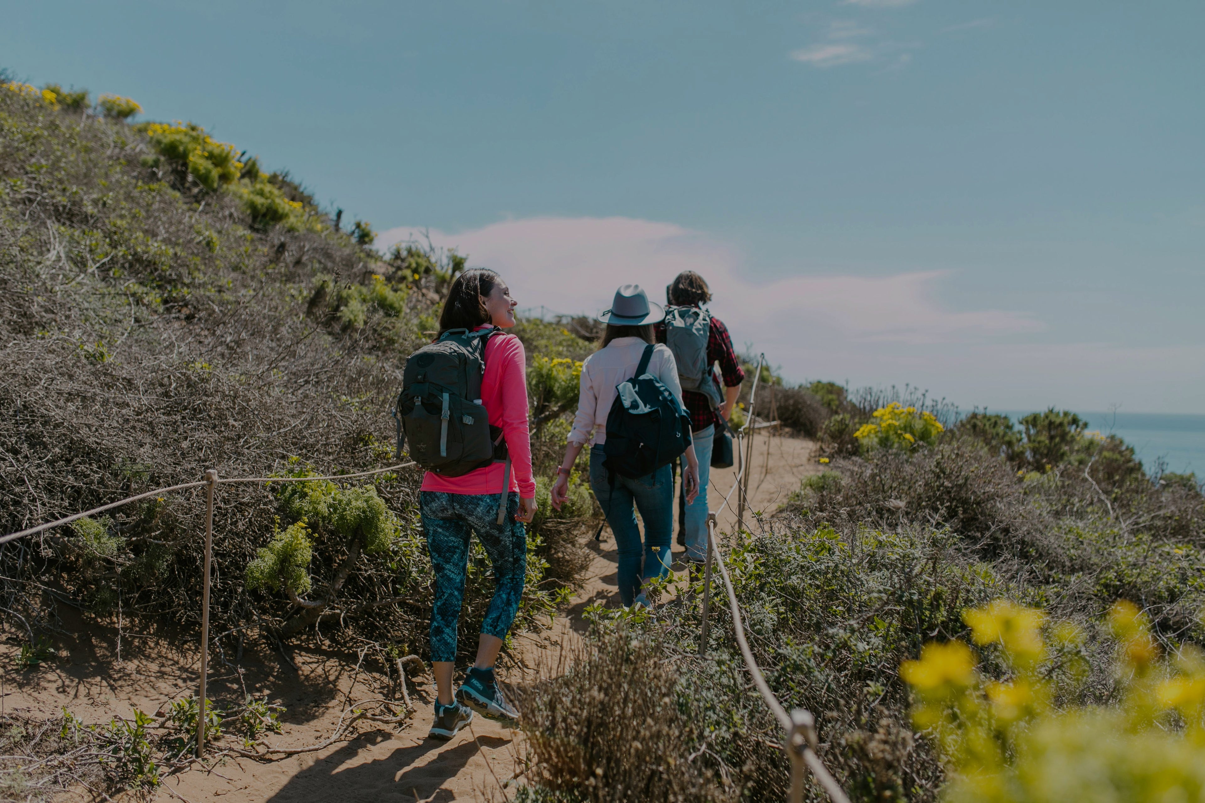 3 people hiking a trail near a beach
